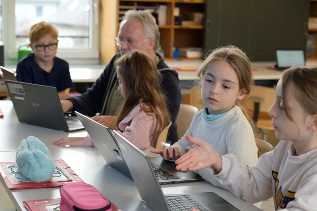 Vier Kinder und ein Mann sitzen vor drei Laptops.