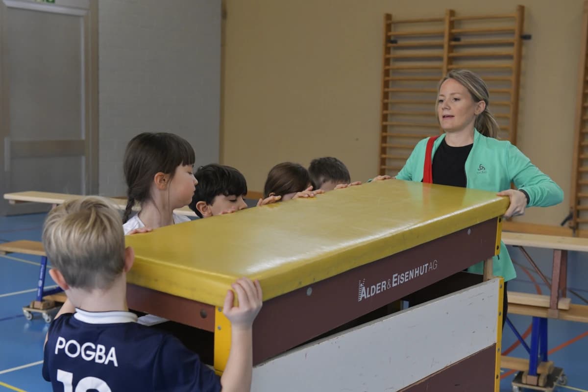 Eine Lehrerin und fünf Kinder tragen einen Kasten.