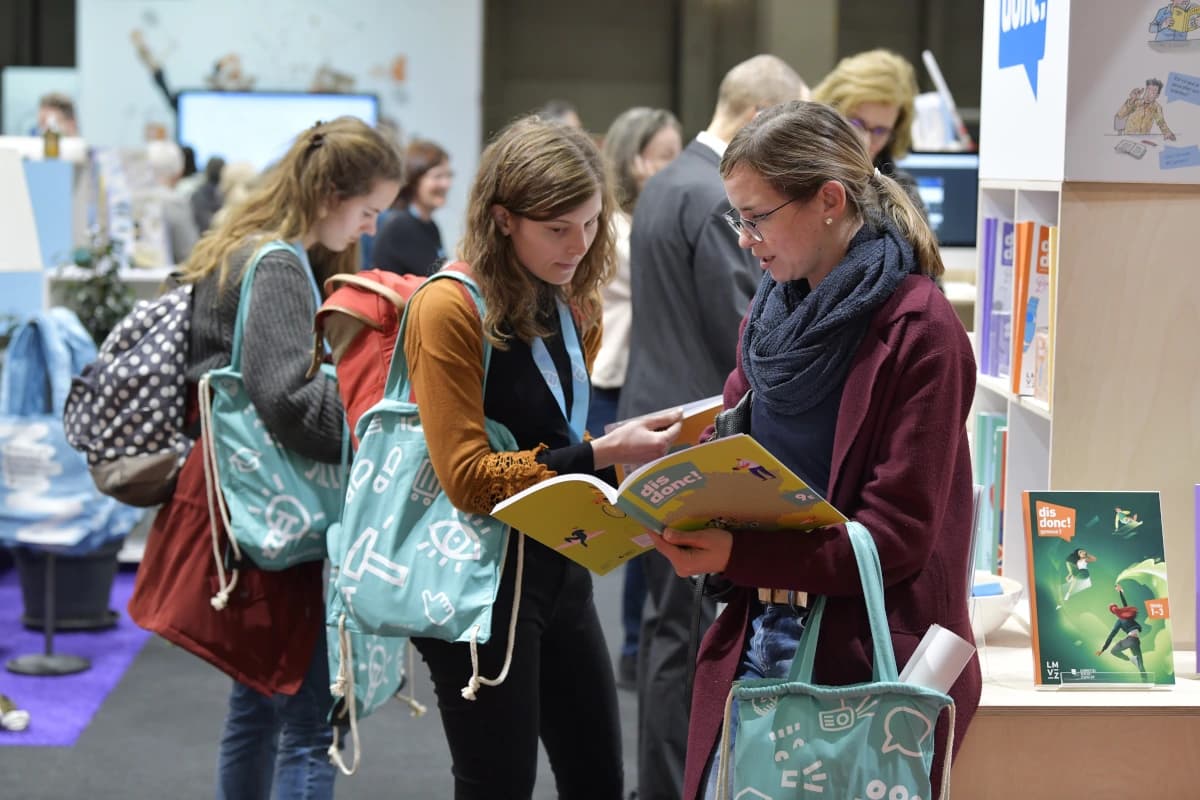 Zwei Frauen schauen gemeinsam ein Buch an, im Hintergrund weitere Personen.