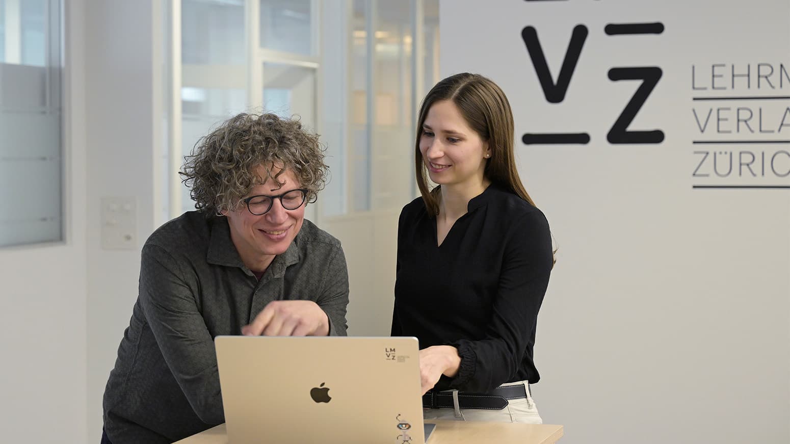 Zwei Personen, die in den Laptop reinschauen und lächeln. 