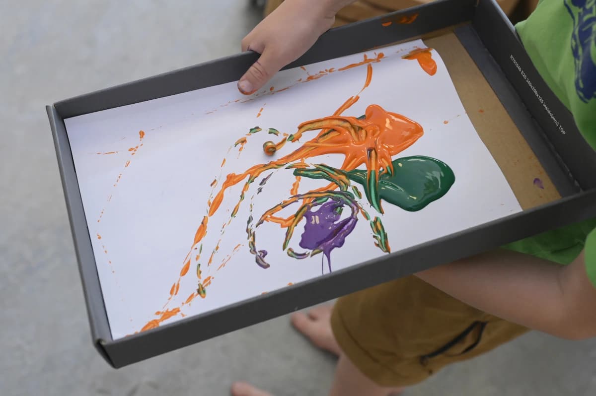 Ein weisses Blatt Papier in einer Kartonschachtel, mit orange, grün und violett wurde auf dem Blatt gemalt.