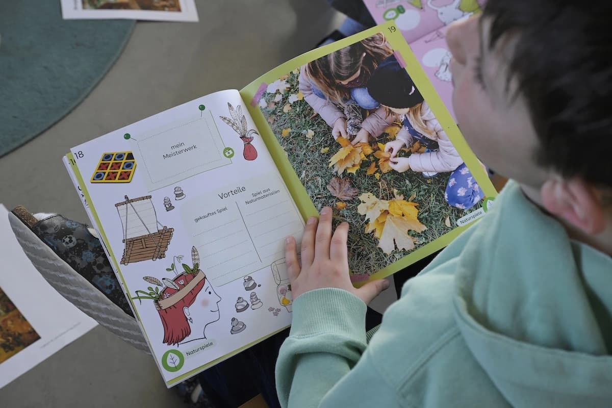 Ein Kind, nur angeschnitten und verschwommen zu sehen, hält ein offenes Lernheft auf seinen Knien.