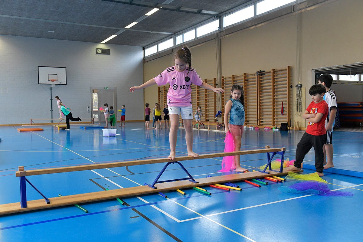 Ein Mädchen balanciert über eine Langbank in der Turnhalle.