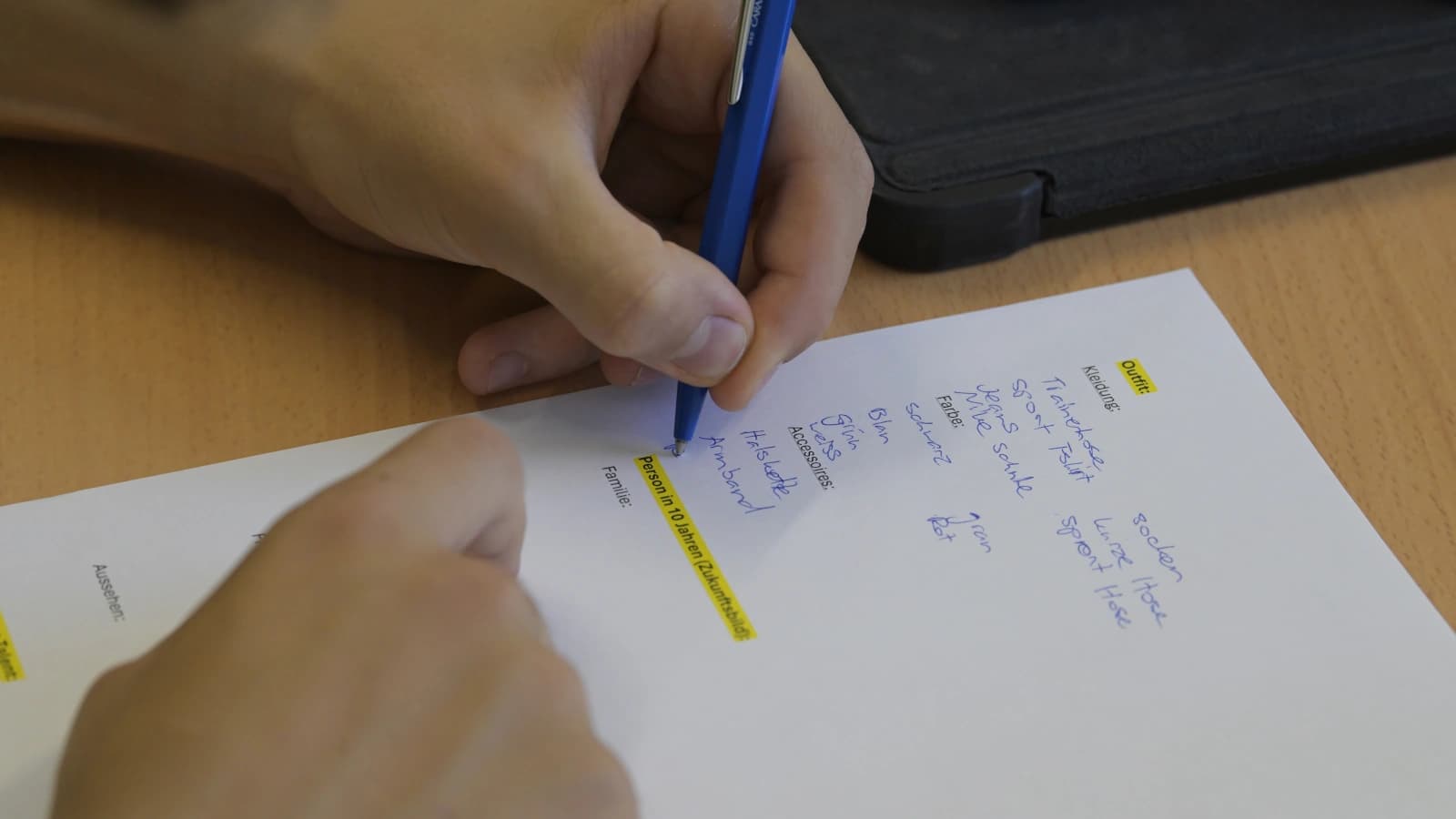 Auf einem weissen Blatt Papier schreibt jemand Begriffe auf. Man sieht nur einen Teil des Papiers, einen Teil der Hände, der einen blauen Kugelschreiber hält.